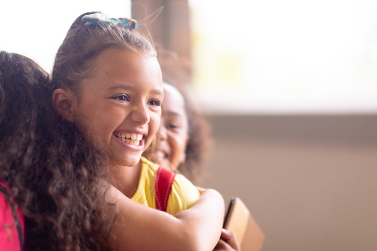 Close-up of multiracial cheerful elementary schoolgirls embracing while standing in school. unaltered, childhood, education and back to school concept.